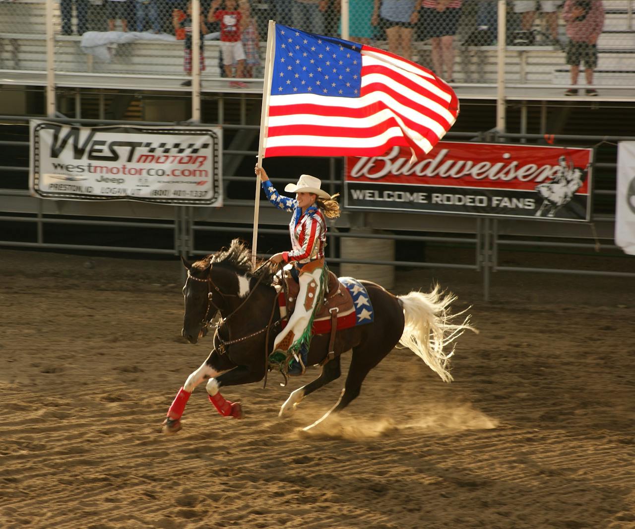 Cowgirl in red, white, and blue rides a horse holding the American flag at a rodeo.